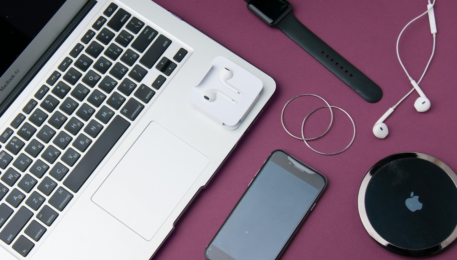 Flat lay of various electronic gadgets on a purple surface including a laptop, smartphone, and smartwatch.