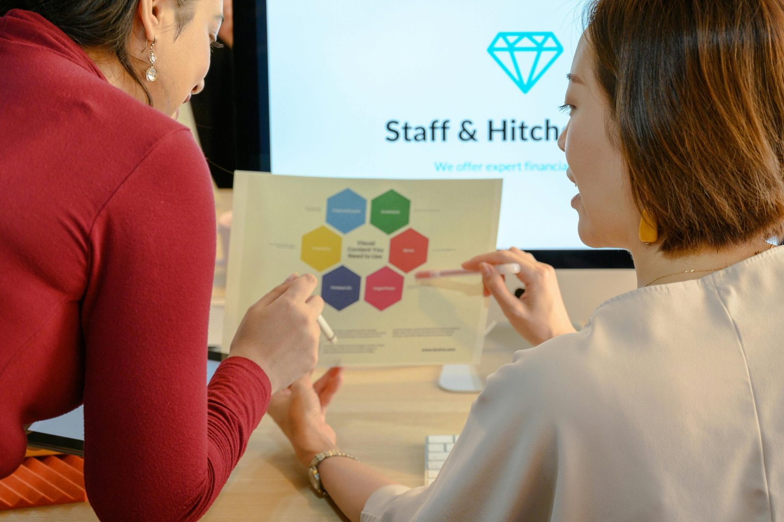 Two women discussing a business project with a color-coded chart in an office setting.